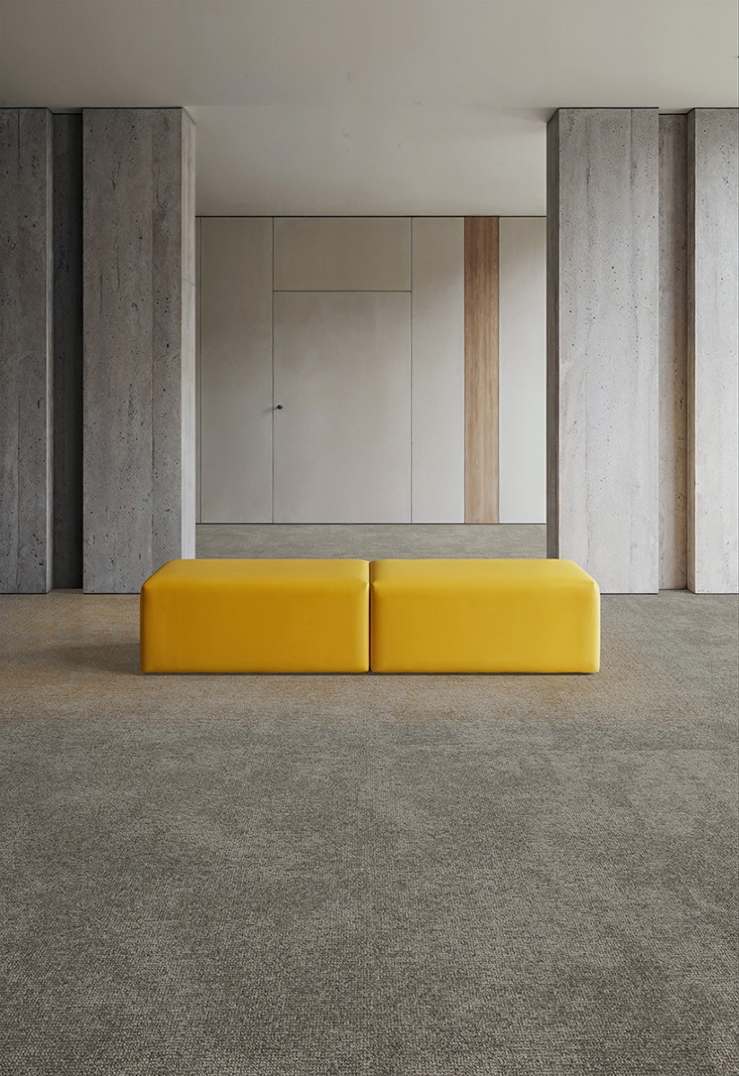 Banca amarilla sobre alfombra modular Glory en corredor de concreto