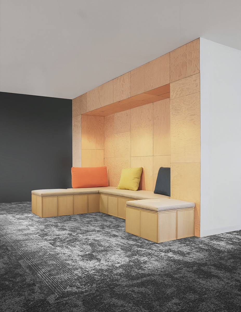 Alfombra modular Glory en tonos grises bajo sala lounge de madera con cojines de color