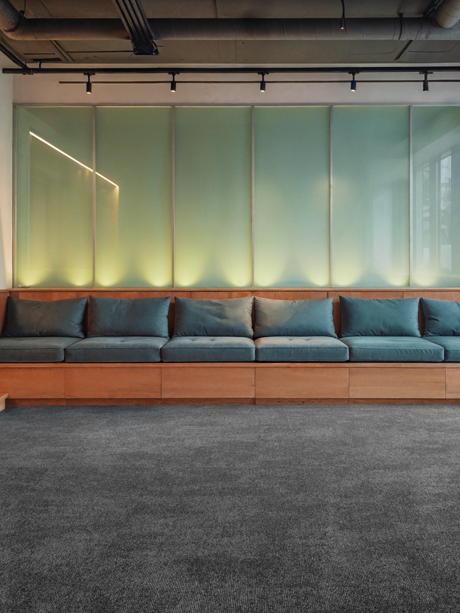 Banca lounge de madera con panel retroiluminado sobre alfombra modular Glory gris